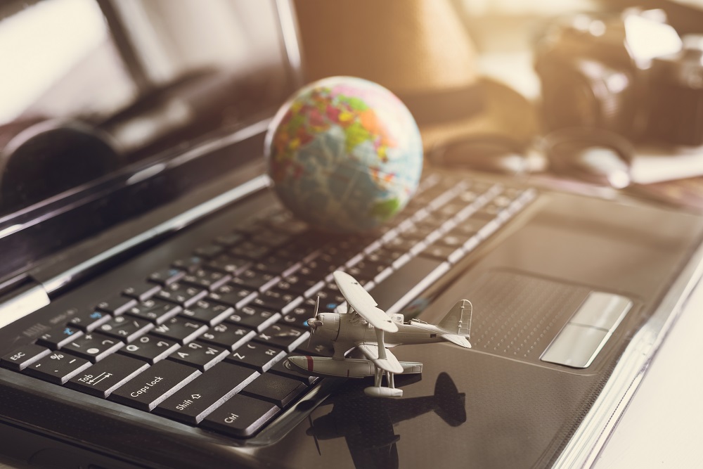 Toy airplane on laptop keyboard with globe and camera Globe on top of laptop with toy airplane