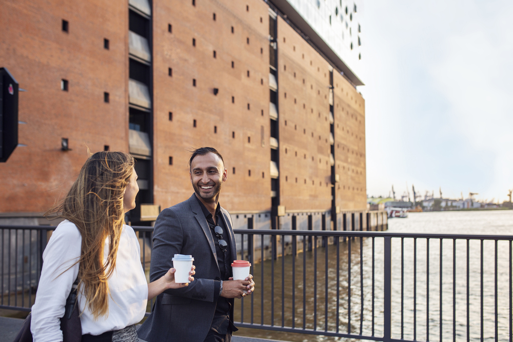 Man and woman walking on bridge by Elbphilharmonie and holding c Man and woman walking on bridge by Elbphilharmonie and holding coffee cups