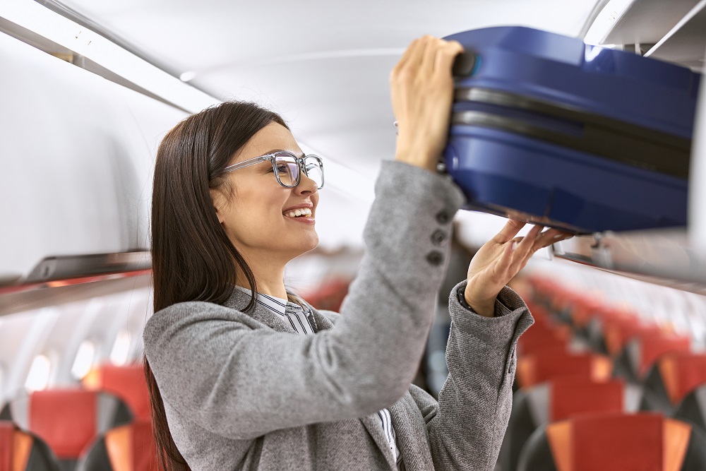 Happy caucasian female passenger with luggage in airplane salon what size is carry-on luggage
