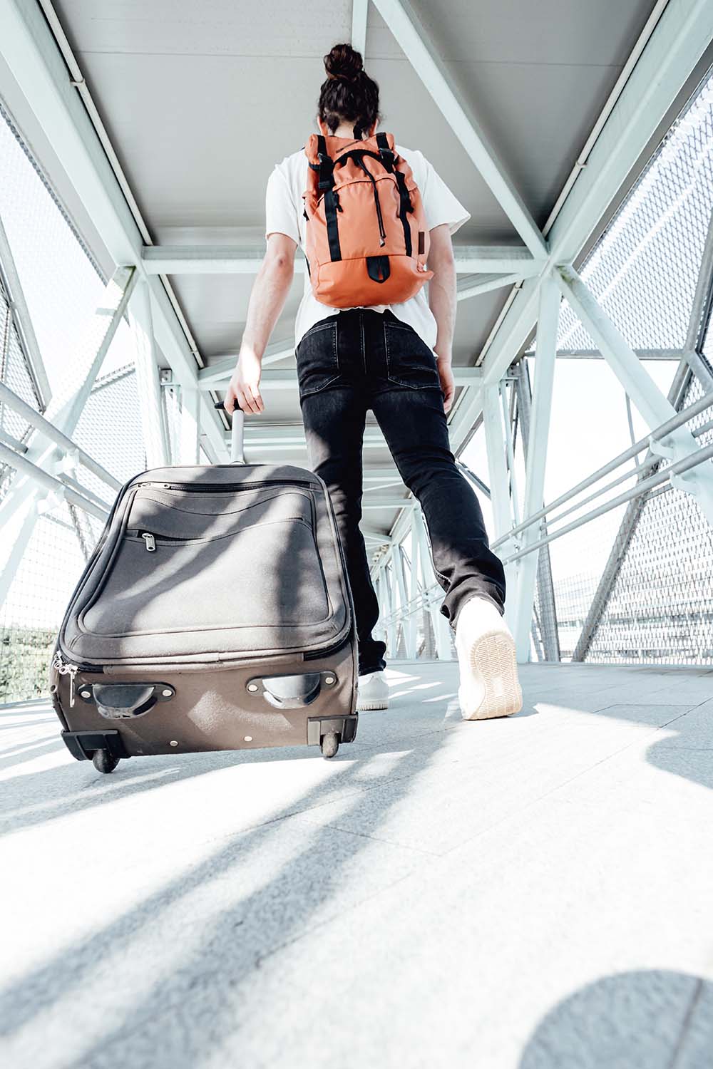 Back shot of a traveler carrying his luggage and bags at the air traveler in airport with backpack and suitcase