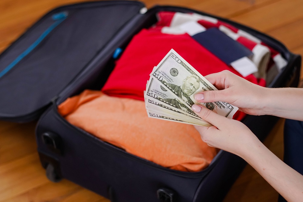 Female hands counting dollar cash banknotes on suitcase background. Woman travel after open boarders. Woman's hands counting dollars in front of a packed suitcase