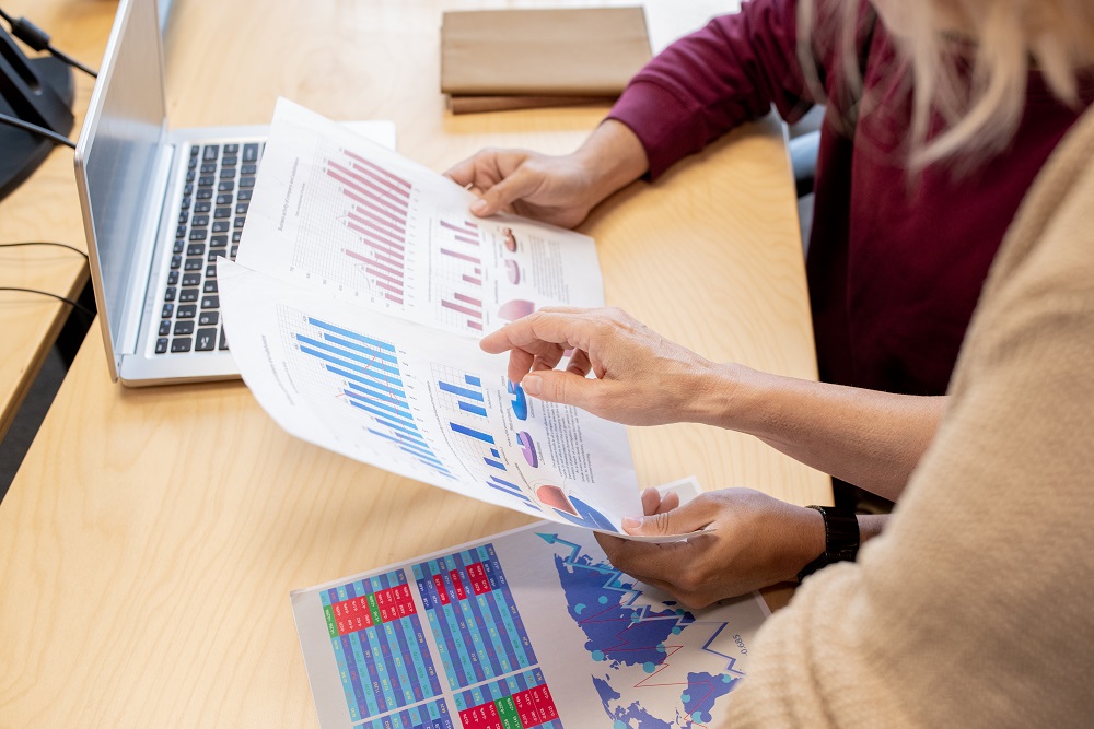 Hand of contemporary female broker pointing at one of financial papers Two people working together to do financial analysis