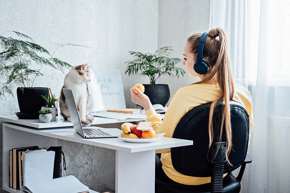 Mental health and work. Work life balance. Young woman in headphones near laptop at home office resting after work. freelancer woman play with cat and eating health food, Taking break time work-life balance