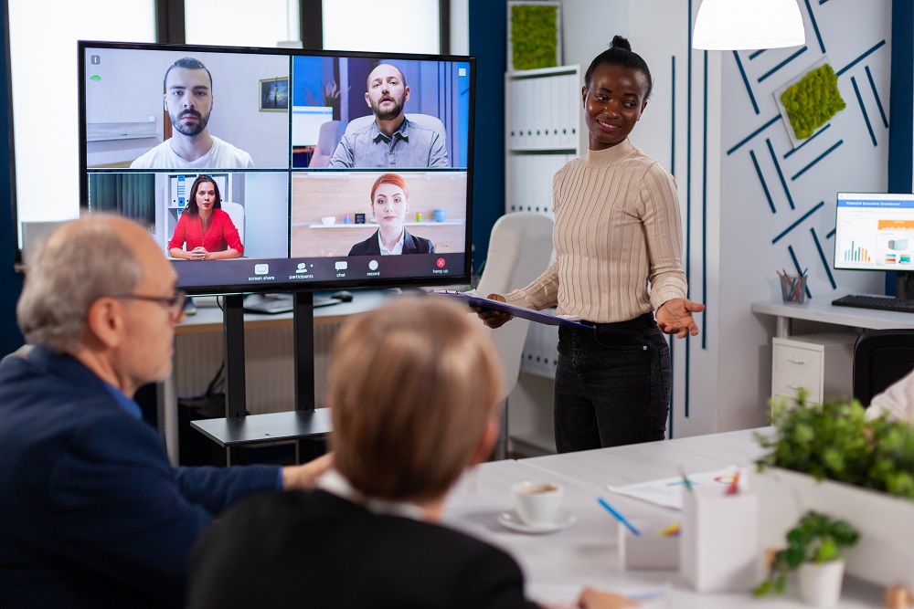 Black manager woman talking with remotely colleagues on Hybrides Meeting mit einer Frau, die in einem Konferenzraum leitet.