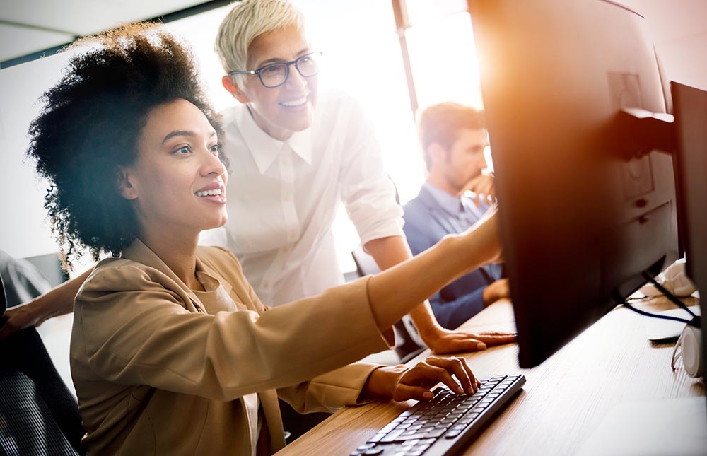 Programmer working in a software developing company Three people at the office with two woman looking at a computer screen