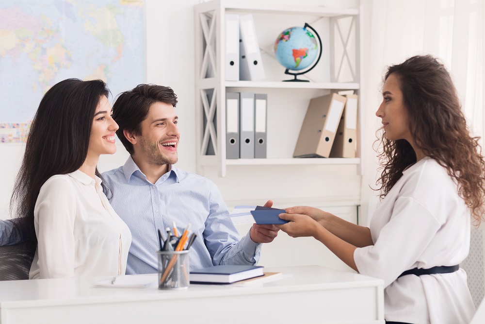 Happy couple getting passports and tickets from tour agent Paar im Reisebüro mit Reisepass