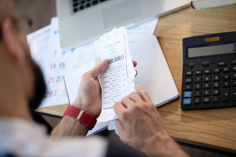 Bearded businessman sitting at the table and working on expenses Geschäftsmann analysiert Reisekosten
