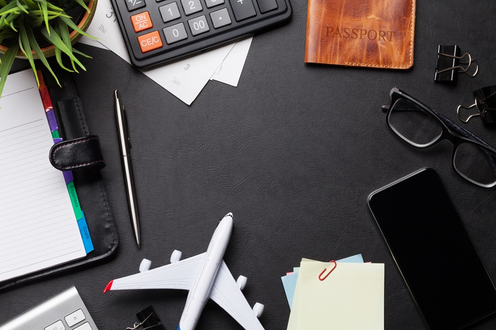 Reisespesen berechnen mit Taschenrechner, Flugzeug, Brille und Agenda auf dem Schreibtisch.