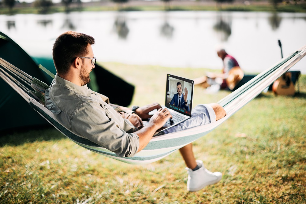 Hello colleague, do you enjoy camping? Man working remotely from a hammock on a video conferencing call