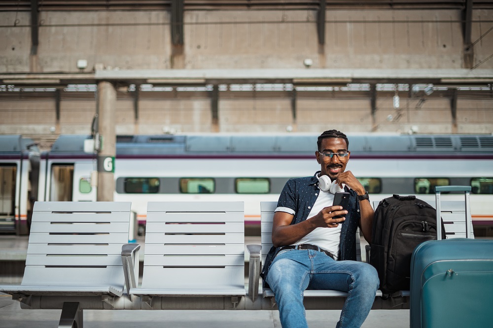 Man using phone at train station Traveler in train station waiting for train with luggage