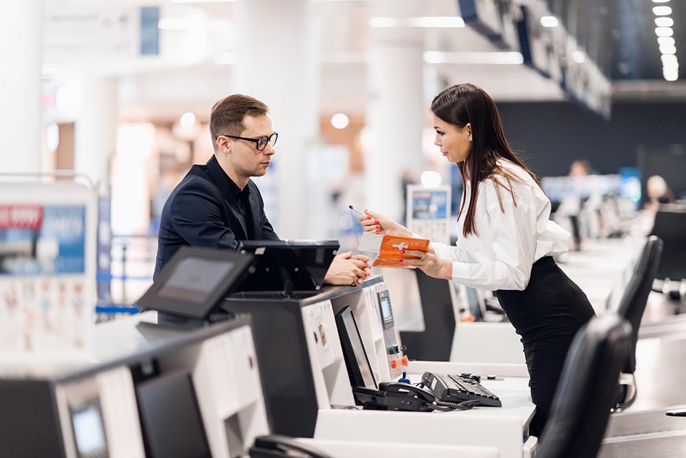 handsome businessman handing over air ticket at airline check in counter Frau am Flughafen, die die Bordkarte von einem Geschäftsreisenden entgegennimmt