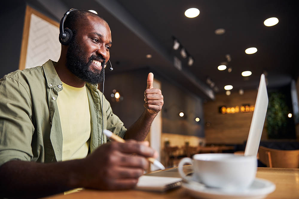 Mann mit Kopfhörern in einem Videoanruf zeigt Daumen hoch