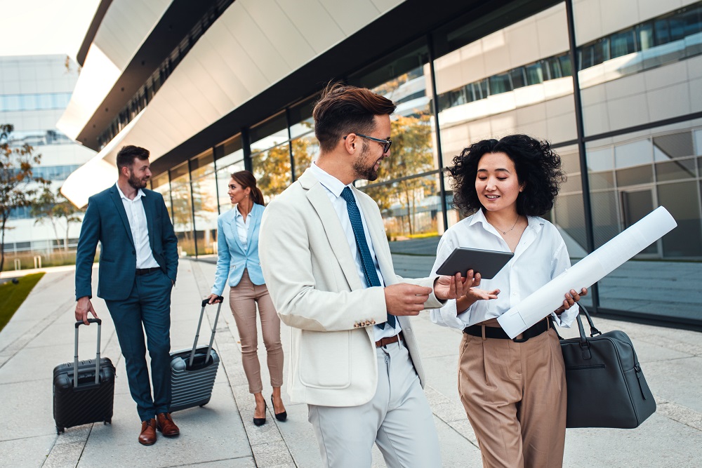 Group of coworkers walking outside in front of office buildings Ein Haufen Kollegen auf einer Dienstreise reden außerhalb vom Büro über ein Projekt.
