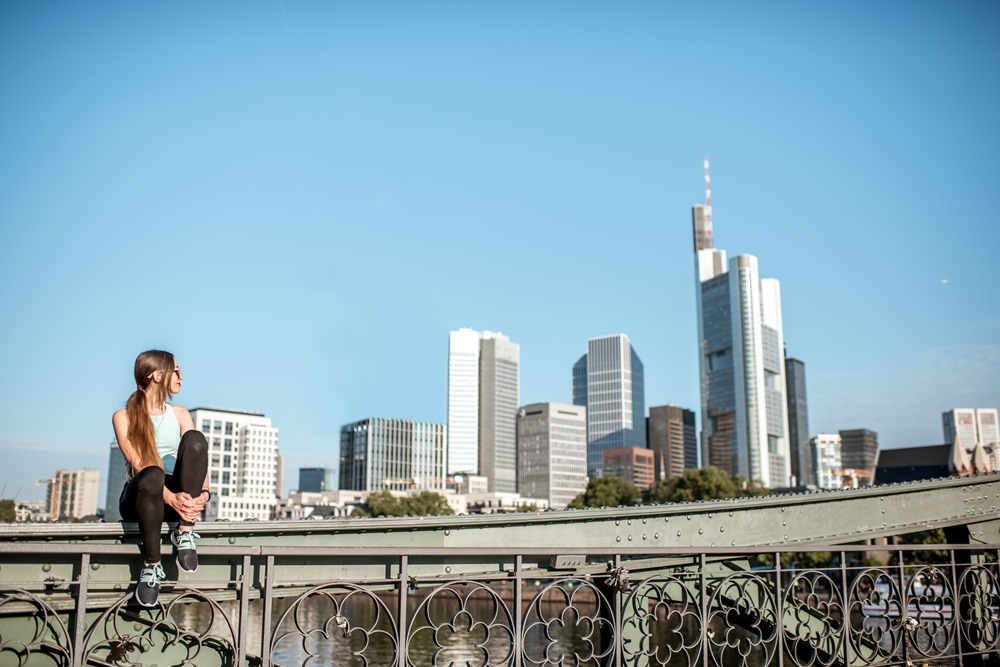 Woman exercising in Frankfurt city Woman sitting on bridge with Frankfurt skyline in background