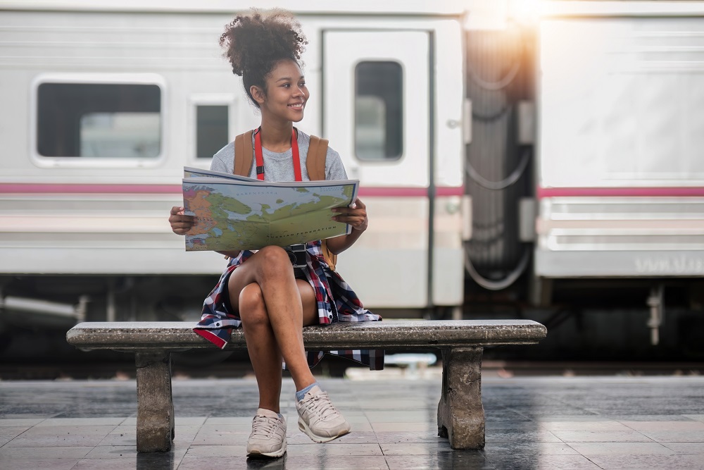 Young woman female smiling traveler with back pack looking to map while waiting for the train at train station. High quality photo woman sitting on a bench at the train station holding a map on a bleisure trip